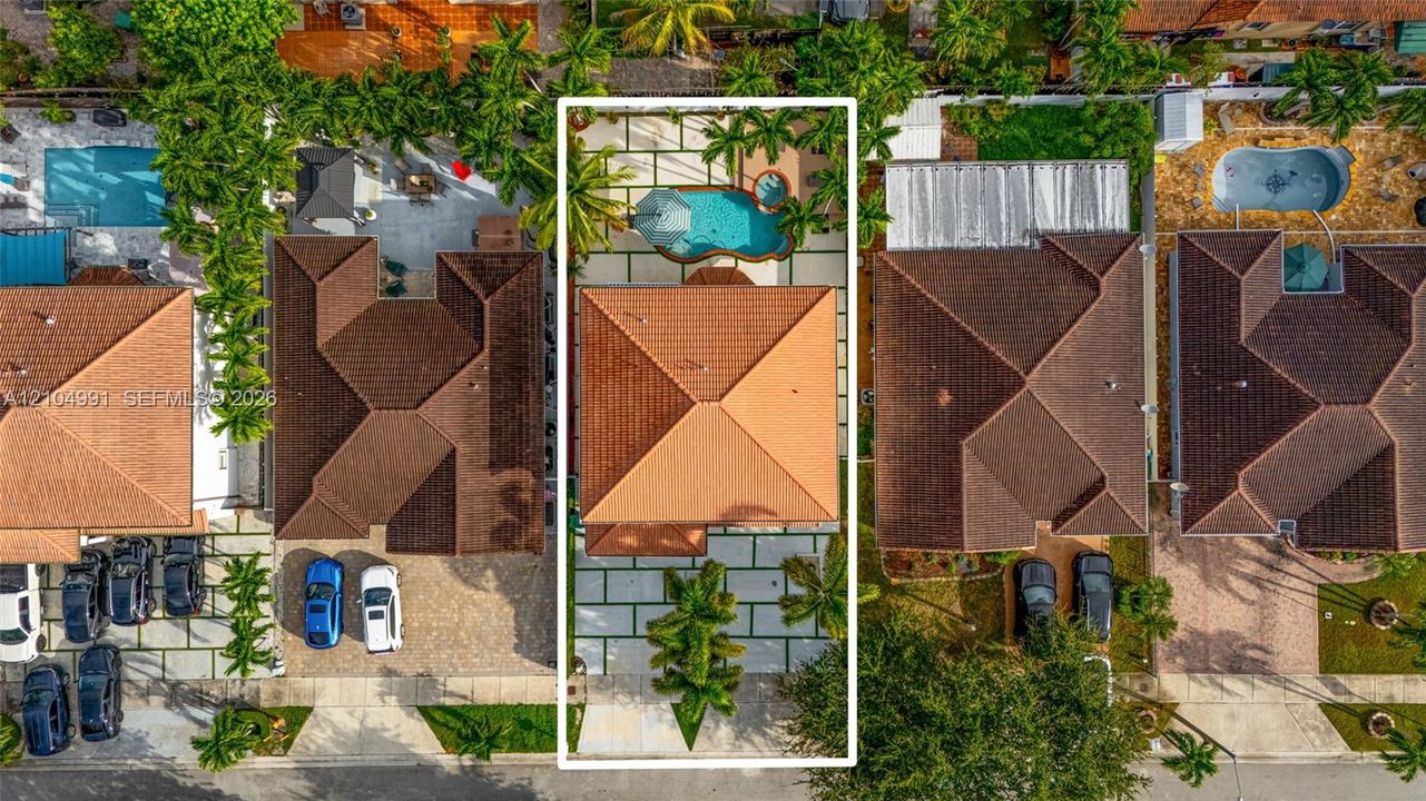 Aerial view featuring a tile roof, paved driveway, pool, built-in spa, and concrete grid hardscaping