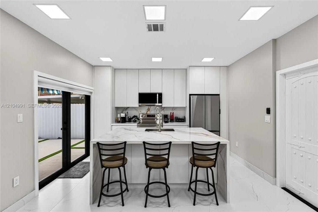 Kitchen featuring floor-to-ceiling cabinetry, a central island with a waterfall-edge countertop, stainless steel appliances, recessed lighting, and large-format tile flooring