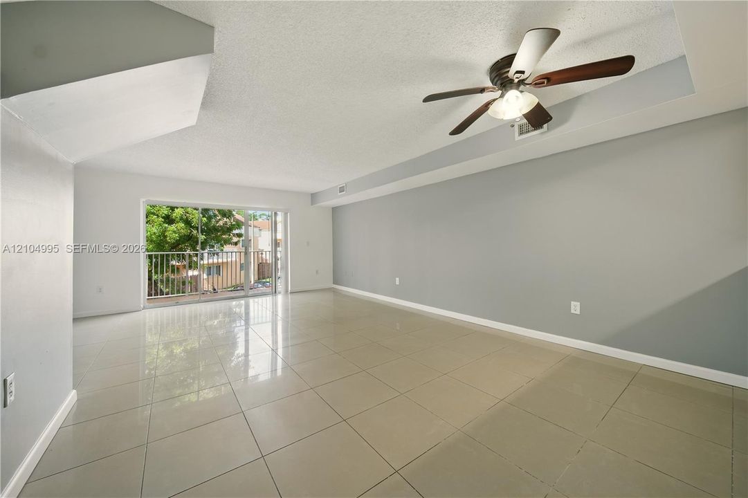 Large-format tile flooring, ceiling fan with integrated light fixture, neutral wall palette, and sliding glass door with external balcony access