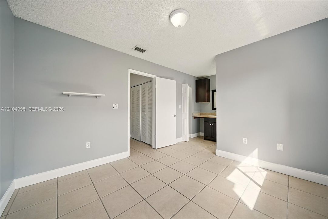 Interior space featuring neutral wall tones, ceramic tile flooring, a mounted display shelf, and a vanity area equipped with dark-finish cabinetry