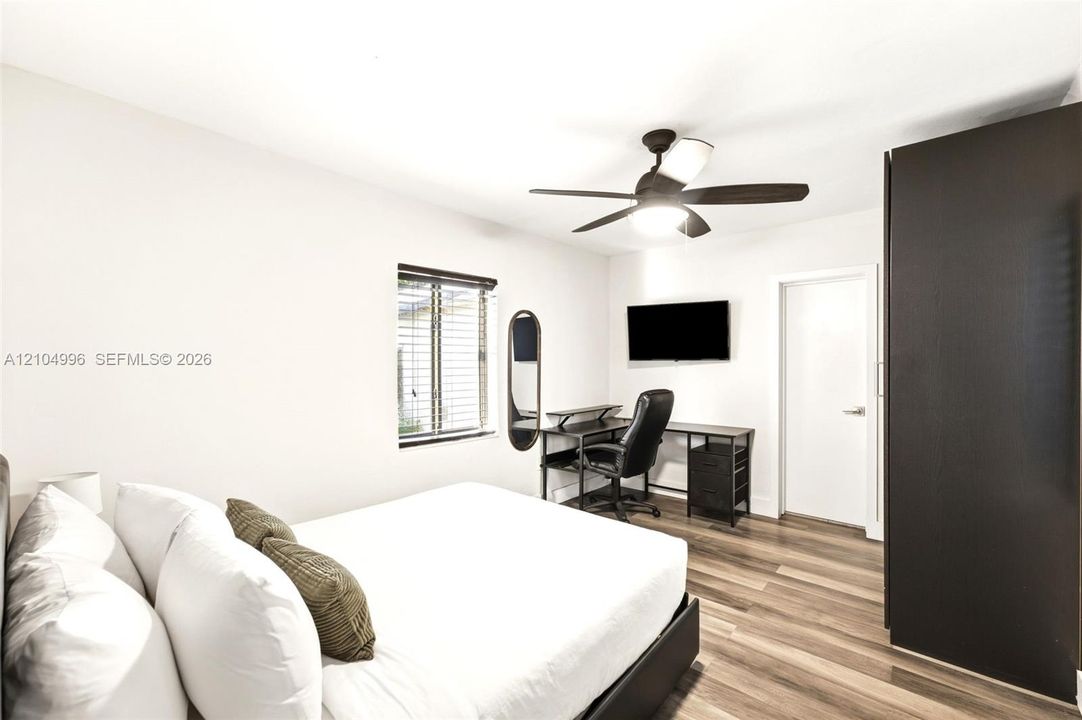 Interior room featuring wood-finish flooring, a ceiling fan with integrated lighting, and a built-in dark cabinetry unit