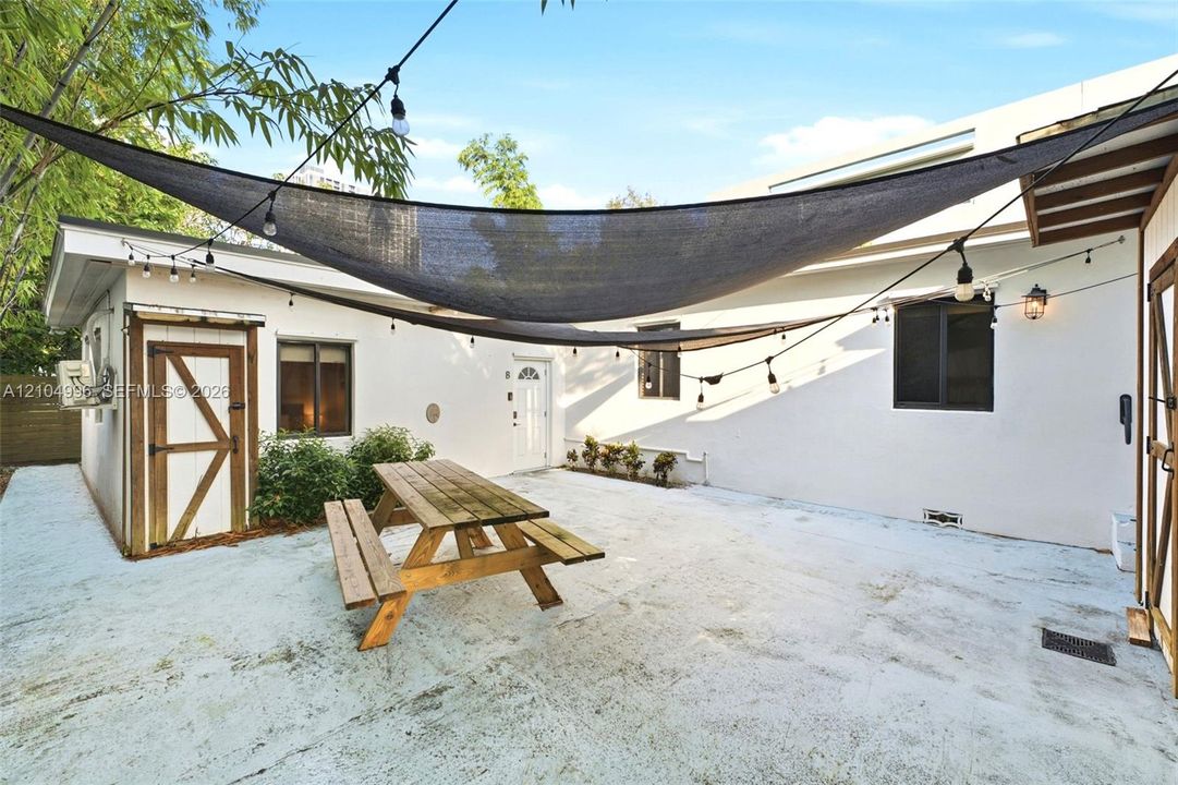 Concrete patio featuring a suspended shade sail, string lighting, and wood-trim exterior storage access