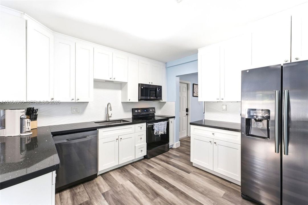 Kitchen featuring white cabinetry, dark stone-finish countertops, textured tile backsplash, stainless steel appliances, and wood-finish flooring