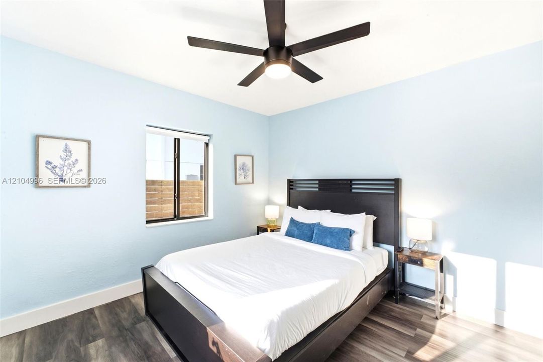Wood-finish flooring, multi-blade ceiling fan with integrated lighting, and single-pane window with dark frame