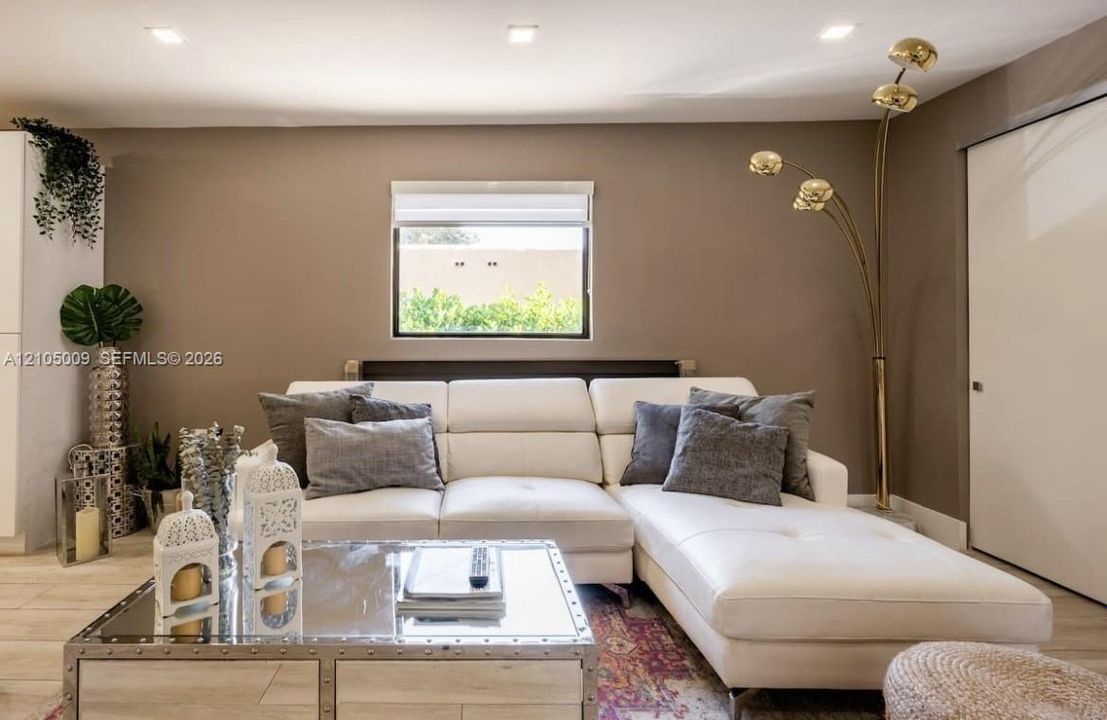 Recessed ceiling lighting, a single window with blinds, and light-toned walls create an inviting living space