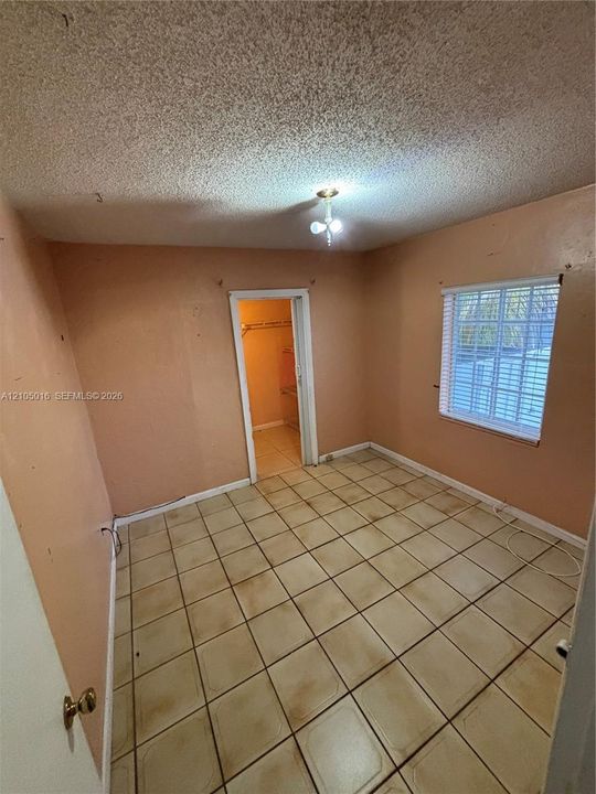 Tile flooring, window with blinds, ceiling-mounted light fixture, open doorway, textured ceiling