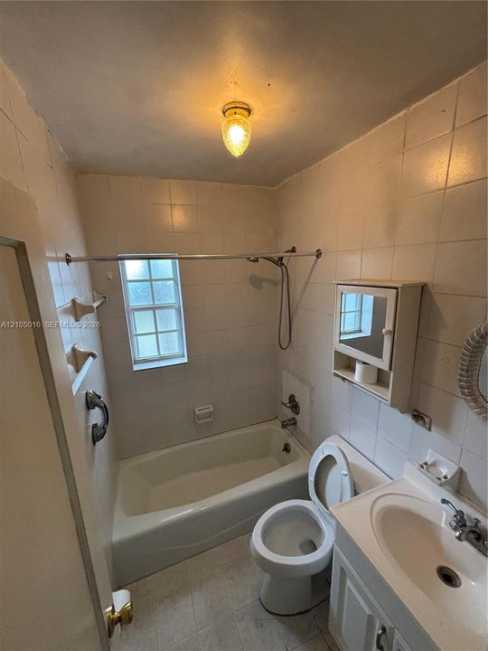 Bathtub with a shower fixture, wall-mounted medicine cabinet, single vanity with integrated sink, and tiled walls