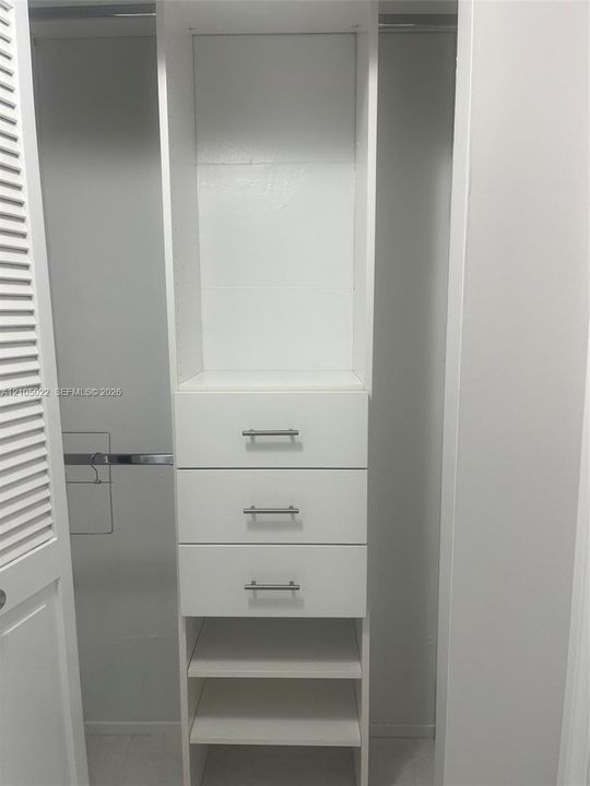 Built-in closet organization system featuring three drawers with brushed nickel pulls, multiple open shelves, and a clothes hanging rod