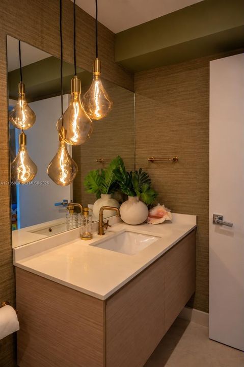 Floating vanity with a light wood-finish cabinet, white countertop, integrated basin, brass-toned hardware, and textured wall covering