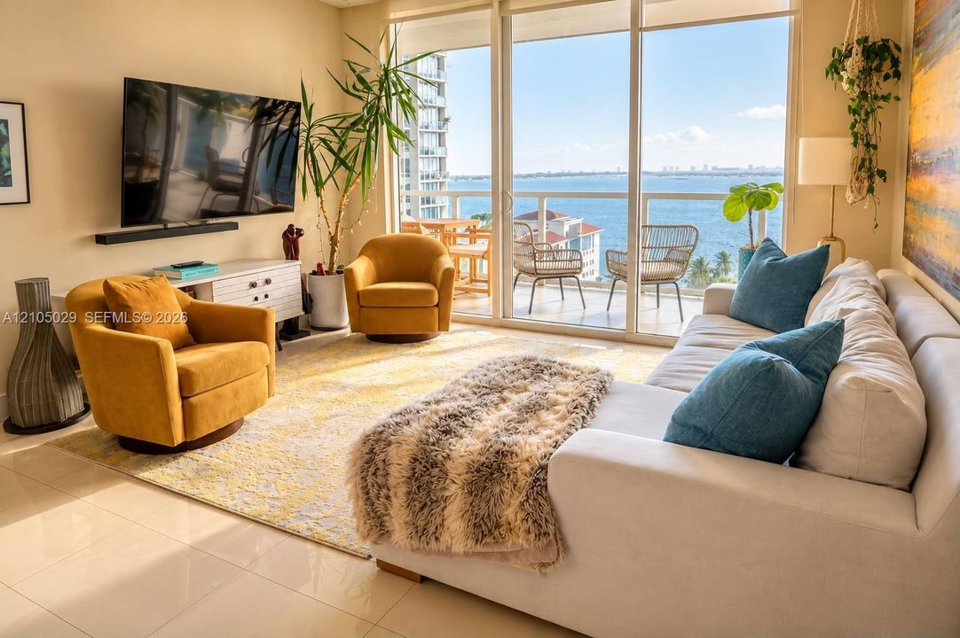 Floor-to-ceiling glass sliding doors, polished tile flooring, balcony with metal railing, and expansive water backdrop