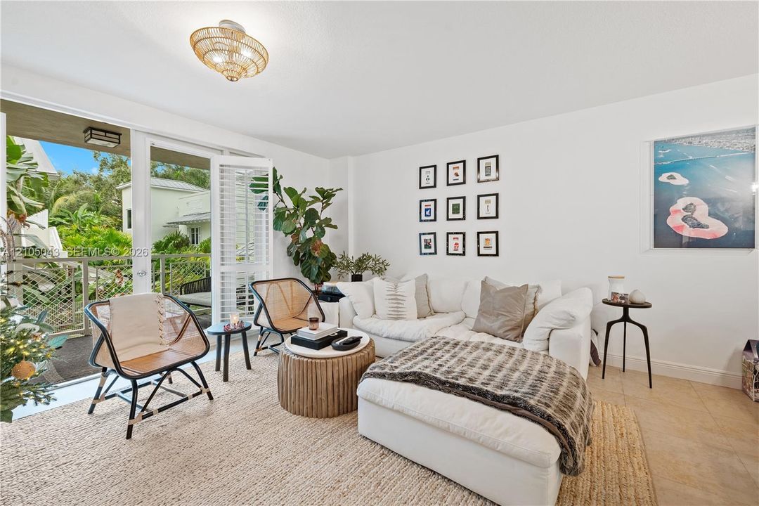 Living area featuring neutral tile flooring, a woven semi-flush mount light fixture, and floor-to-ceiling glass doors opening to a covered balcony with metal railing