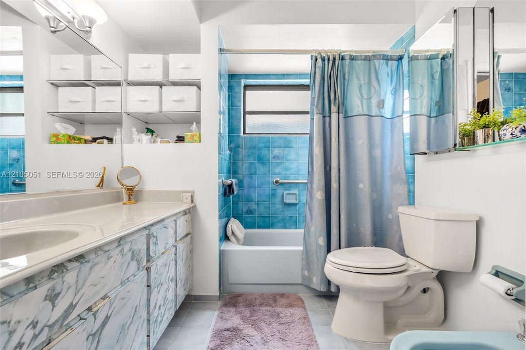 Bathroom featuring a vanity with integrated sink and stone-patterned cabinetry, blue tile tub surround, inset shelving, and a wall-mounted mirrored medicine cabinet