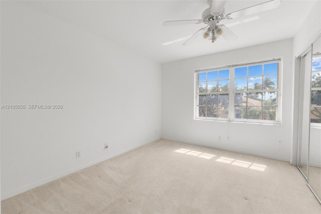 3rd Bedroom - Neutral-toned carpeting, multi-pane window, white-finish ceiling fan with integrated lighting, and a mirrored sliding closet door