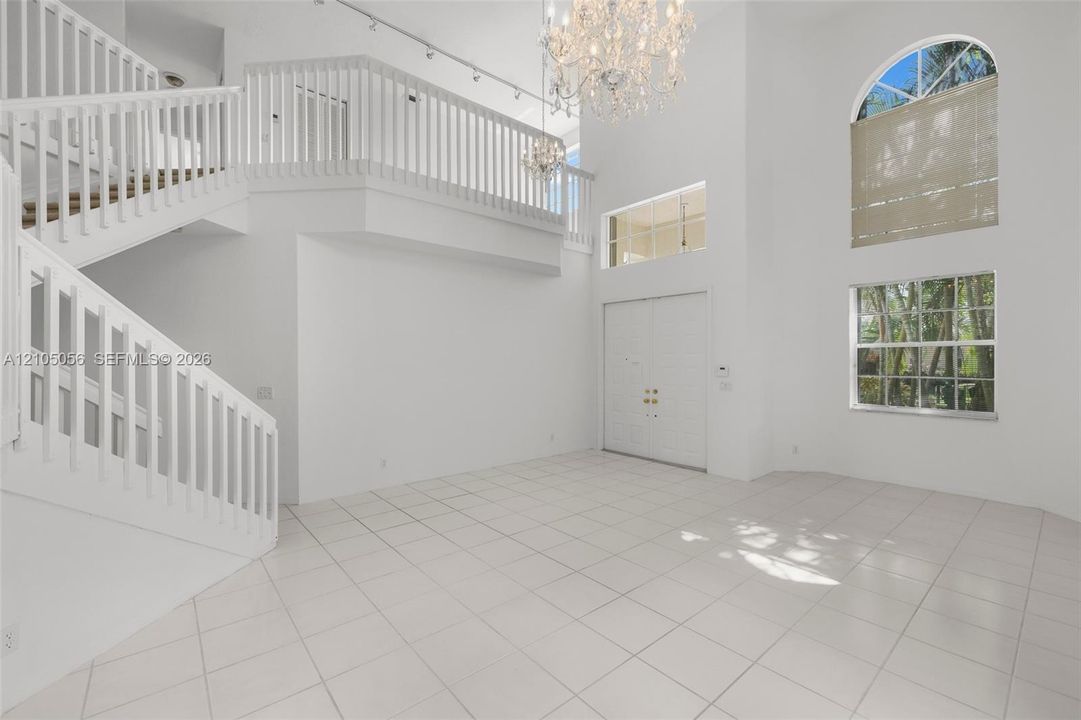 Two-story foyer featuring high ceilings, a grand crystal chandelier, large-format tile flooring, a multi-level staircase with white railings, and arched transom windows