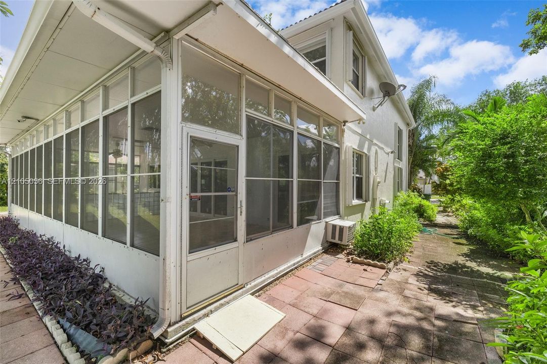Screened-in patio featuring a paver stone walkway, white metal framing, and a dedicated landscape garden bed