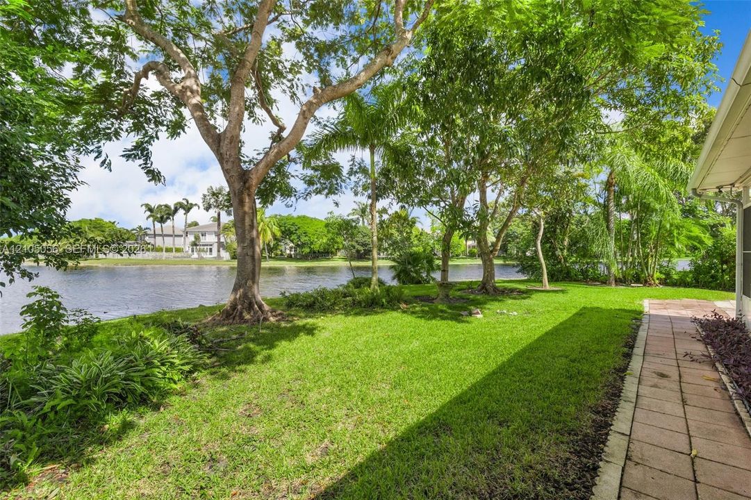 Waterfront backyard featuring mature shade trees, established landscaping, and a paver walkway