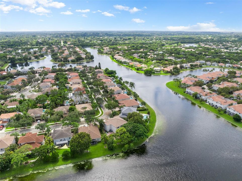 Aerial perspective of a waterfront residential community featuring expansive canal frontage, lush mature landscaping, winding paved streets, and tile-roofed housing