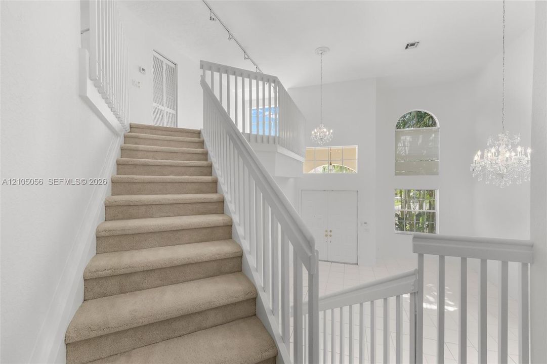 Stairs view to Grand foyer featuring a high ceiling, dual crystal chandeliers
