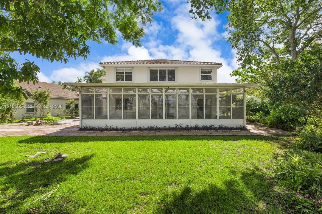 Two-story exterior featuring a screened-in ground-level porch, neutral stucco finish, multi-pane windows, and a hipped roofline set against a grass lawn