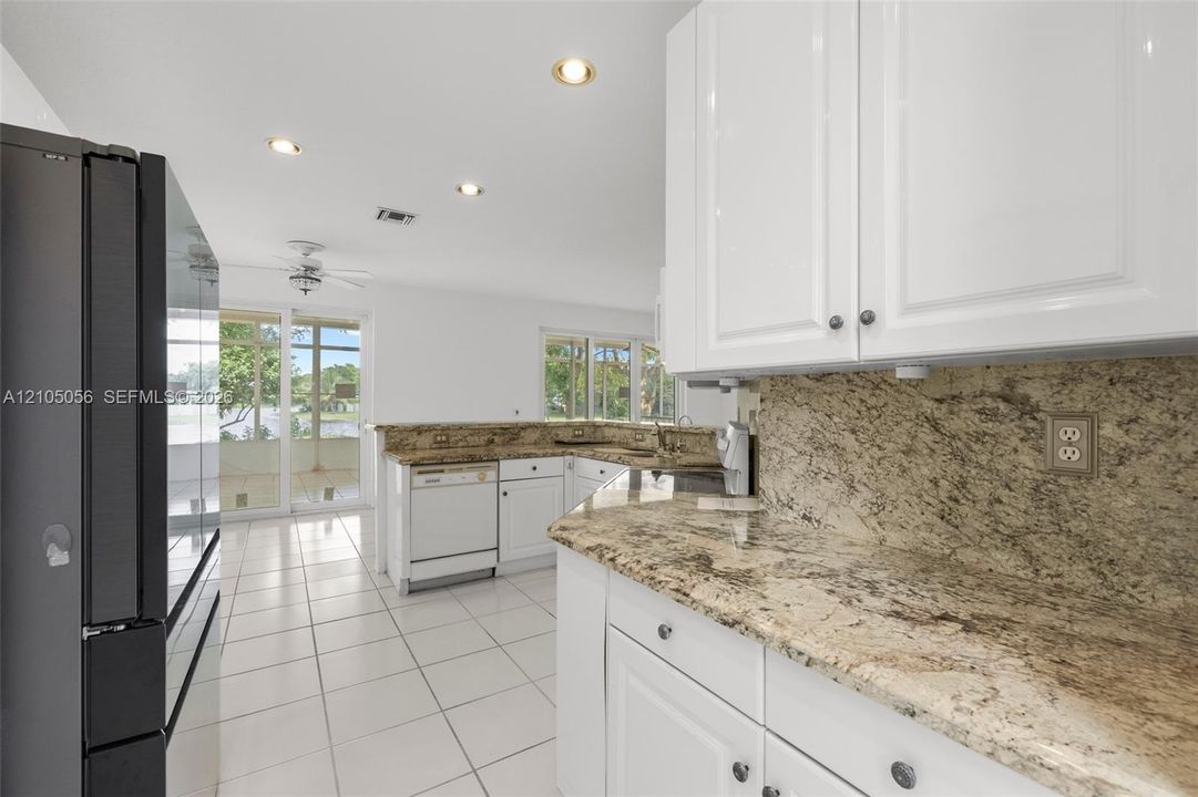 Kitchen featuring white cabinetry, stone countertops, tiled flooring, recessed lighting, and a white dishwasher with views to the lake.