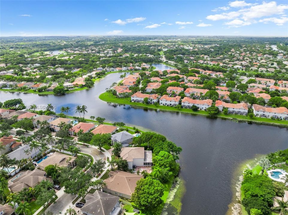 Aerial view of residential community featuring waterfront parcels, mature canopy trees, winding streets, and residential structures with tile roofing