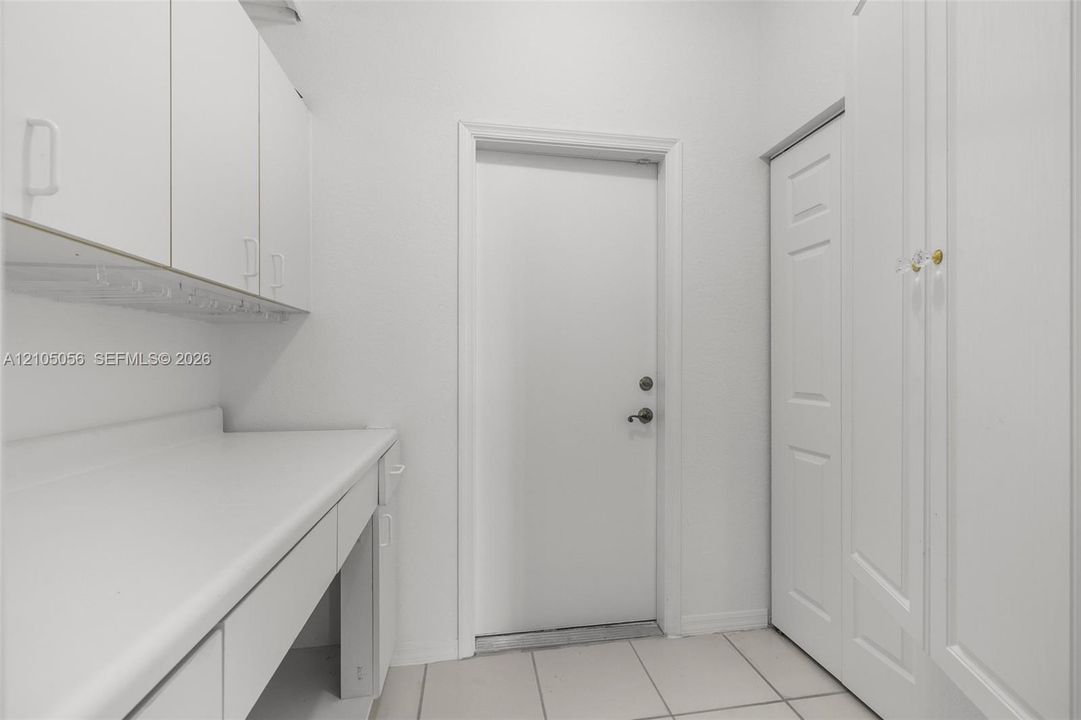 Utility area featuring white built-in cabinetry, solid-surface countertop, floor-to-ceiling storage closet, and tile flooring leads to the 3 car garage to house your toys
