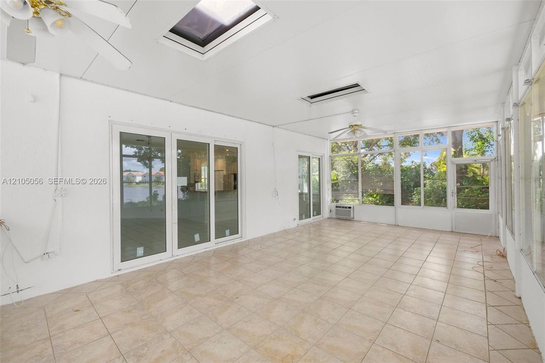 Enclosed patio featuring tile flooring, dual skylights, white walls, ceiling fans, and expansive glass sliding doors