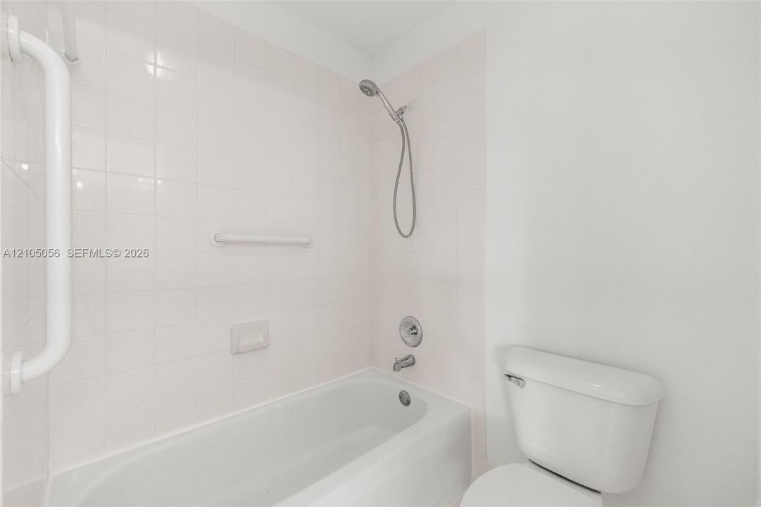 2nd upstairs bathroom Bathtub and shower combination with white tile surround, chrome fixtures, and wall-mounted safety bars