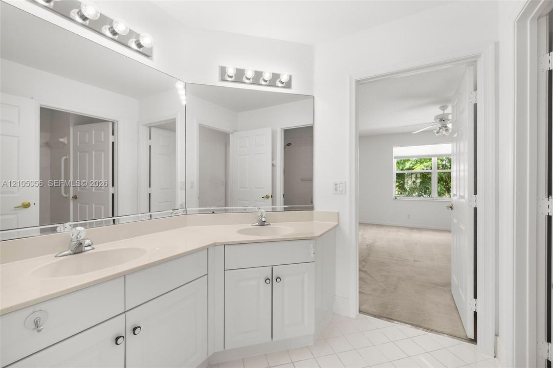 Bathroom vanity with solid-surface countertop, dual integrated sinks, and polished chrome fixtures, featuring a large wall-to-wall mirror and overhead light fixtures