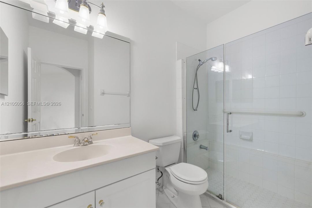 Downstairs Bathroom featuring a vanity with an integrated basin, a large wall-mounted mirror, a four-bulb light fixture, and a tile-surround shower with a glass door