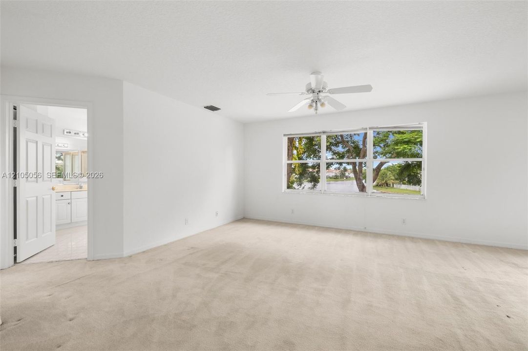 Neutral-toned carpeted flooring, white interior walls, ceiling fan with integrated lighting, multi-pane window with exterior greenery and views to the lake