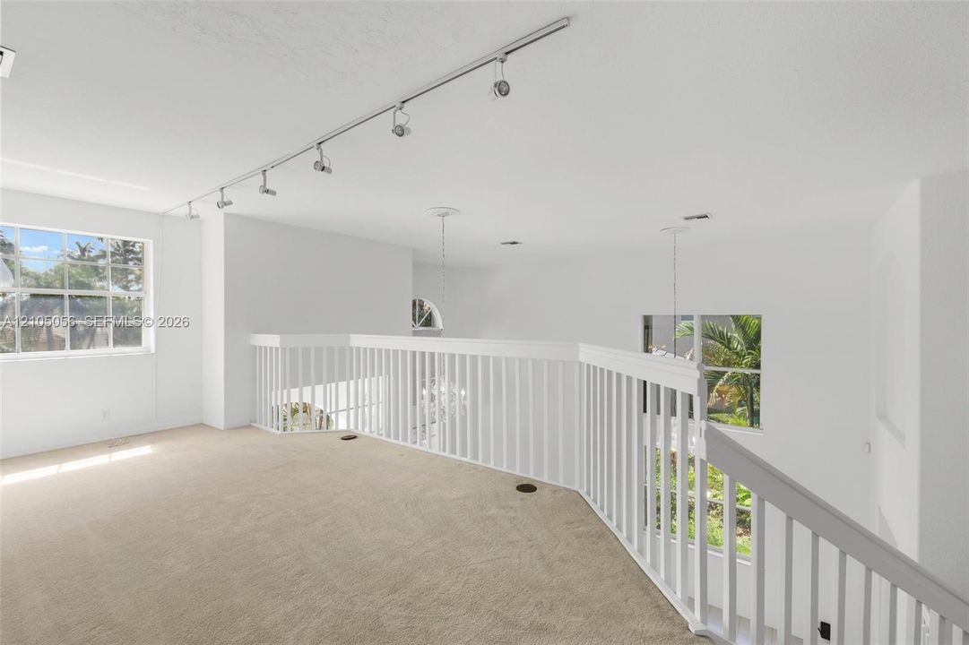 Open mezzanine area featuring wall-to-wall carpeting, white railing, adjustable track lighting, and grid-patterned windows - great area to suit your needs