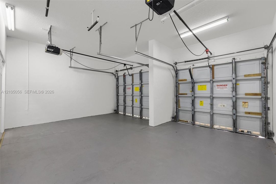 Attached two-car garage featuring painted walls, concrete flooring, and overhead fluorescent lighting