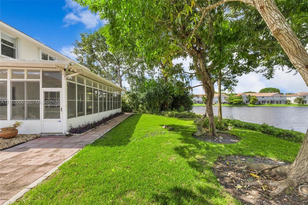 Screened-in patio with concrete paver flooring, expansive grass lawn, mature trees, and waterfront shoreline