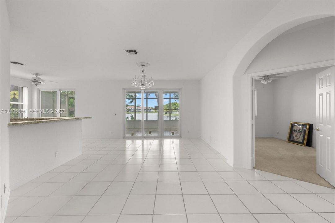 Open-concept interior featuring large-format tile flooring, a stone-surfaced breakfast bar, a decorative chandelier, multi-panel sliding glass doors with views to the lake, , and a grand arched doorway leading to the downstairs bedroom