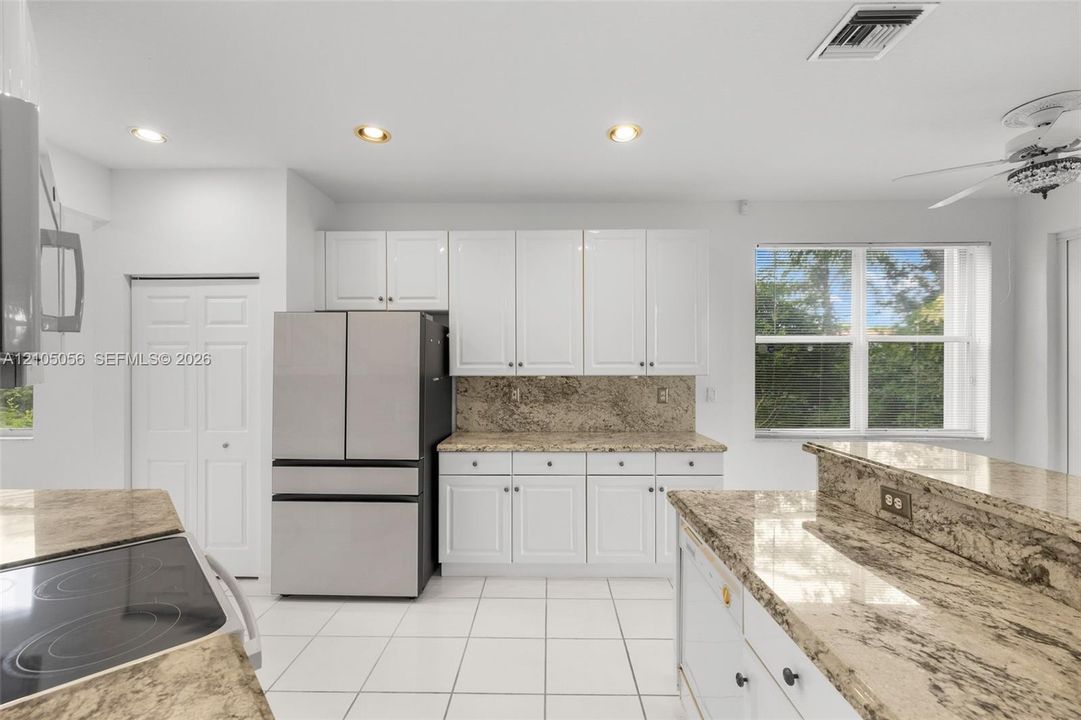 Kitchen featuring white cabinetry, stone countertops, stainless steel refrigerator, white tile flooring, and recessed lighting