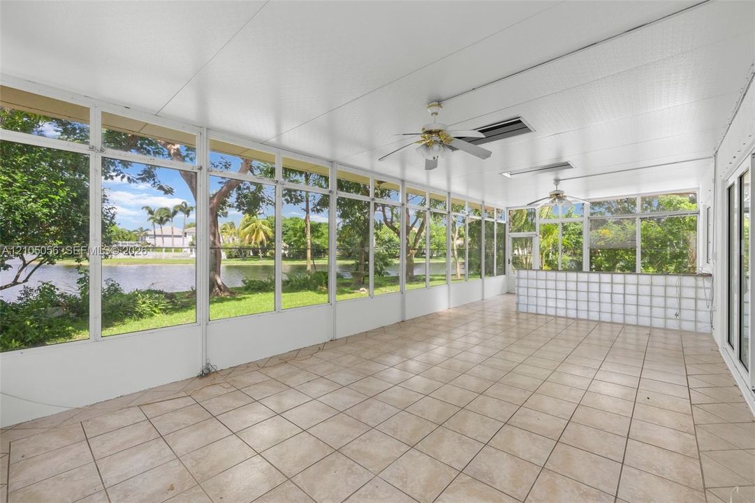 Screened lanai featuring tile flooring, ceiling fans, glass block wall, and panoramic water frontage