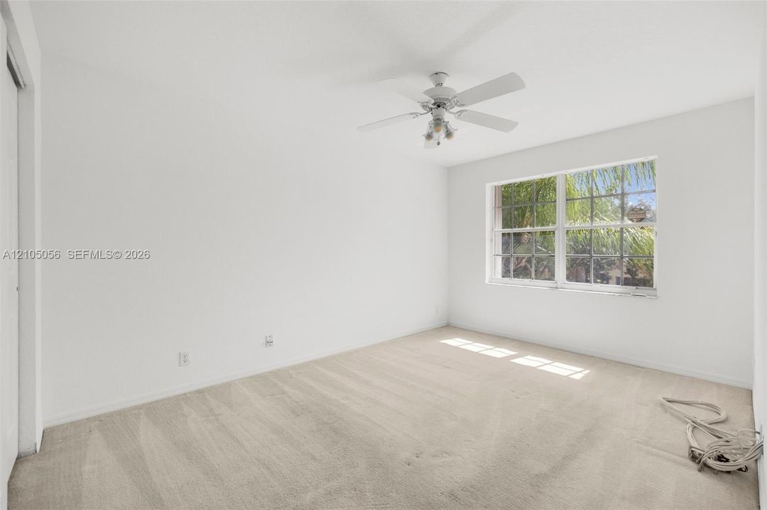 2nd Bedroom - Neutral-toned carpeting, white walls, grid-pattern window, and a multi-blade ceiling fan with integrated light fixture