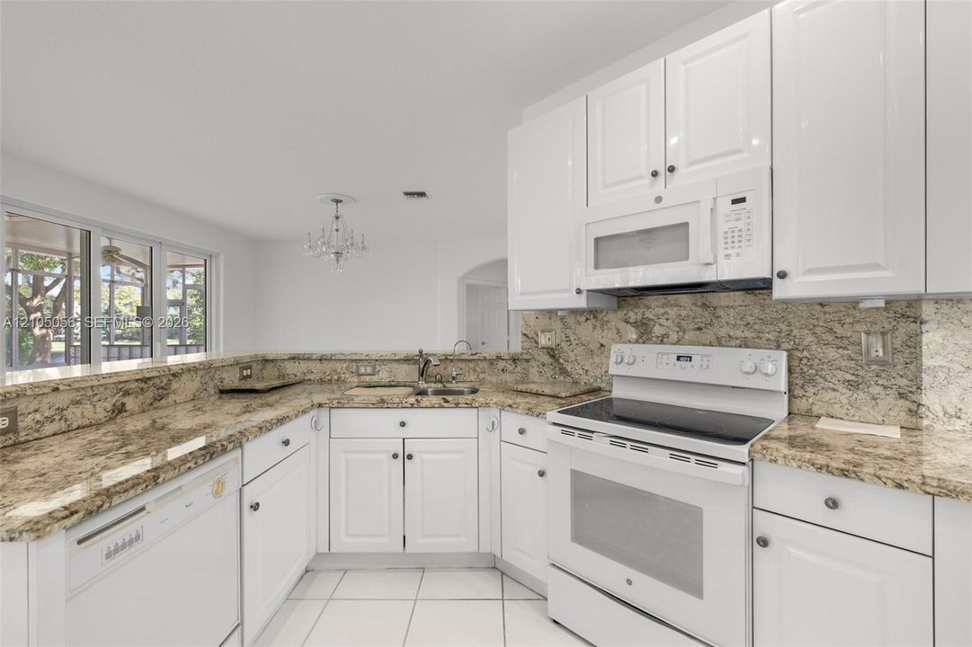 Kitchen featuring white cabinetry, stone-finish countertops, tile flooring, built-in white appliances, and a pass-through opening great for entertaining.