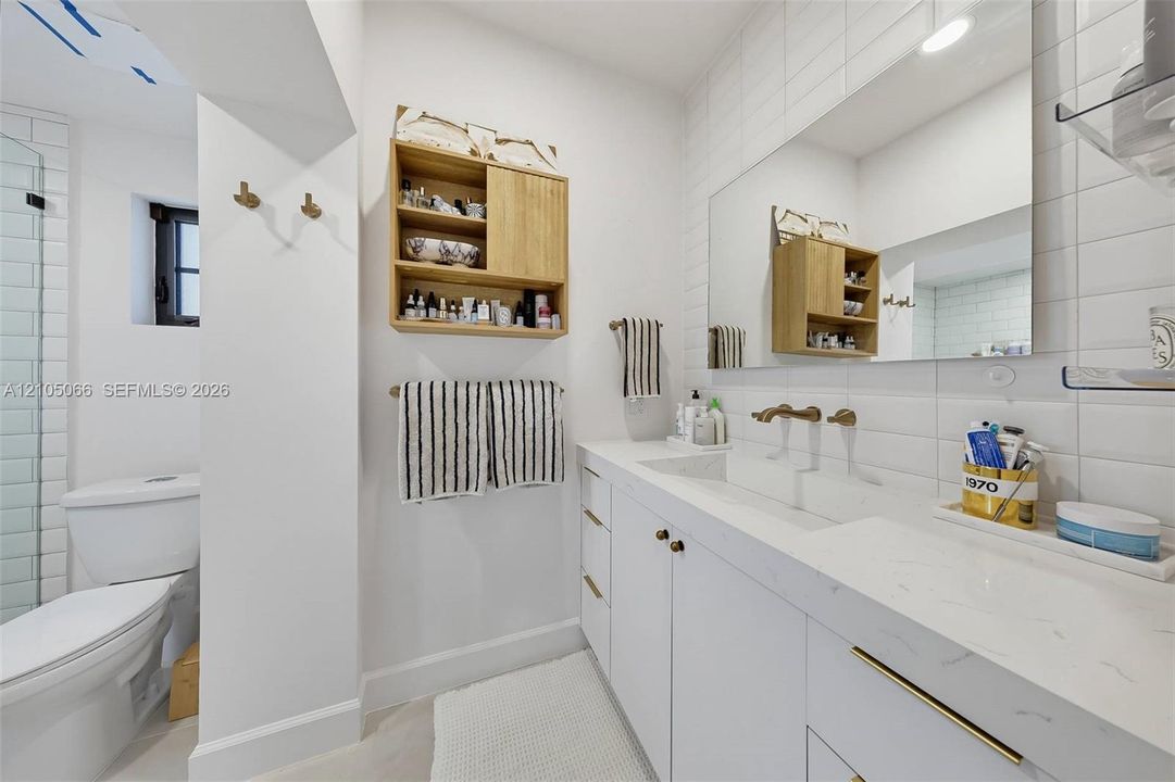 Bathroom featuring a white vanity with integrated double sinks, quartz countertop, brass-tone hardware, wall-mounted faucets, and subway tile wall surrounds