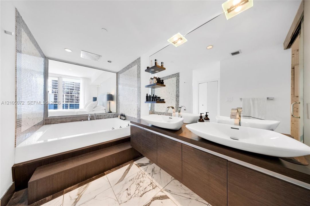 Primary bathroom with built-in tub, two vessel sinks, and a long wood-toned vanity.