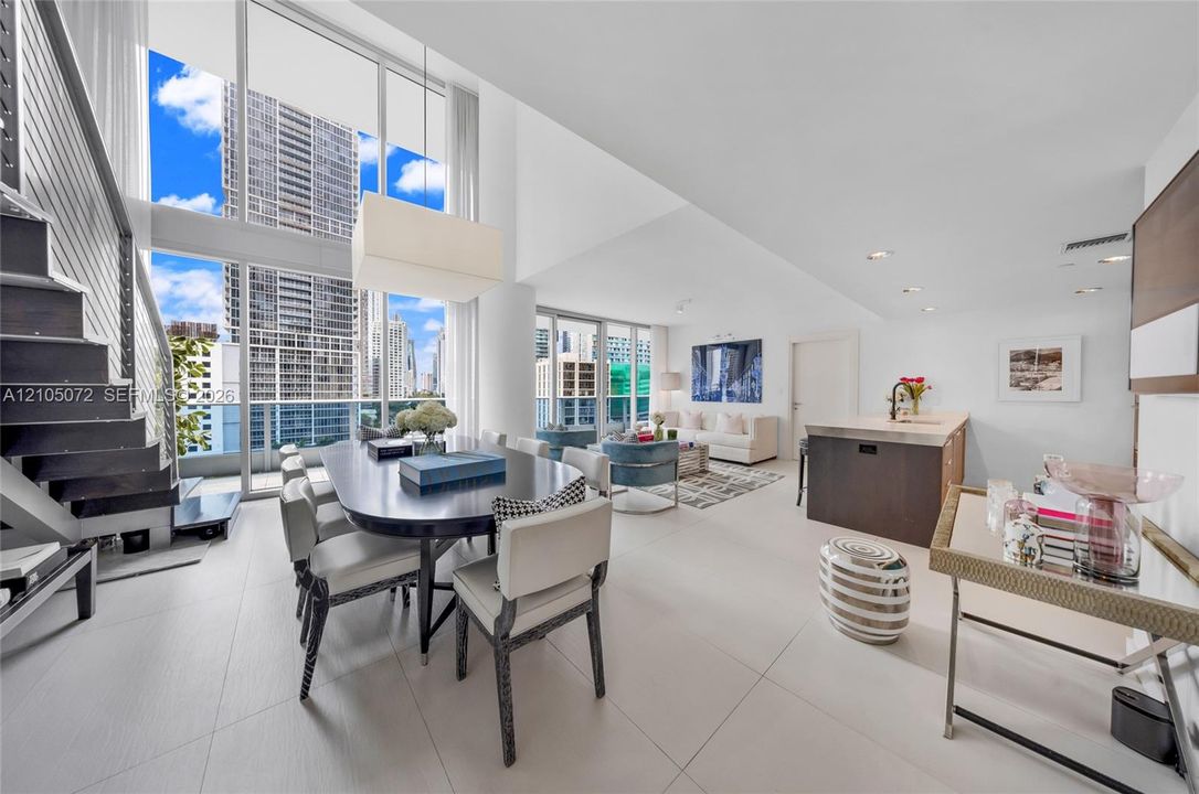 Two-story loft dining area with tall windows, open staircase, and connected living space.