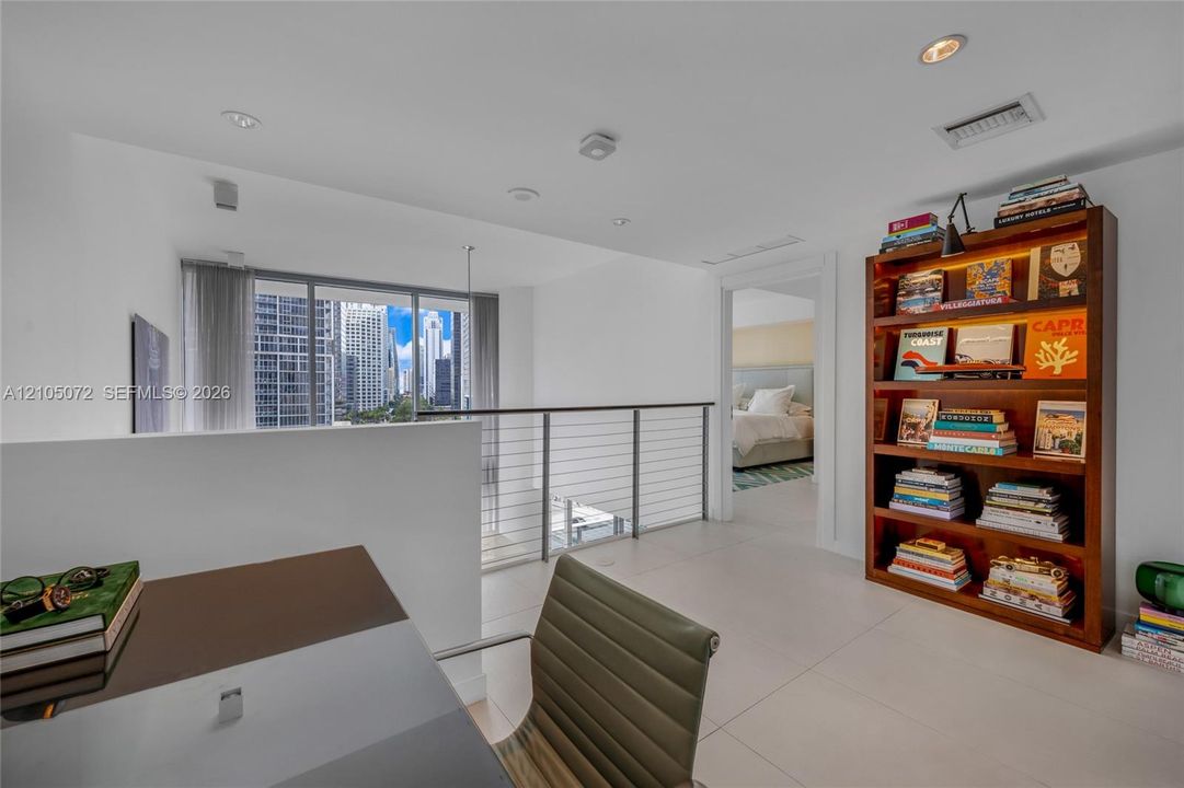 Upper-level den with desk, bookcase, cable railing, and passage to the primary bedroom.