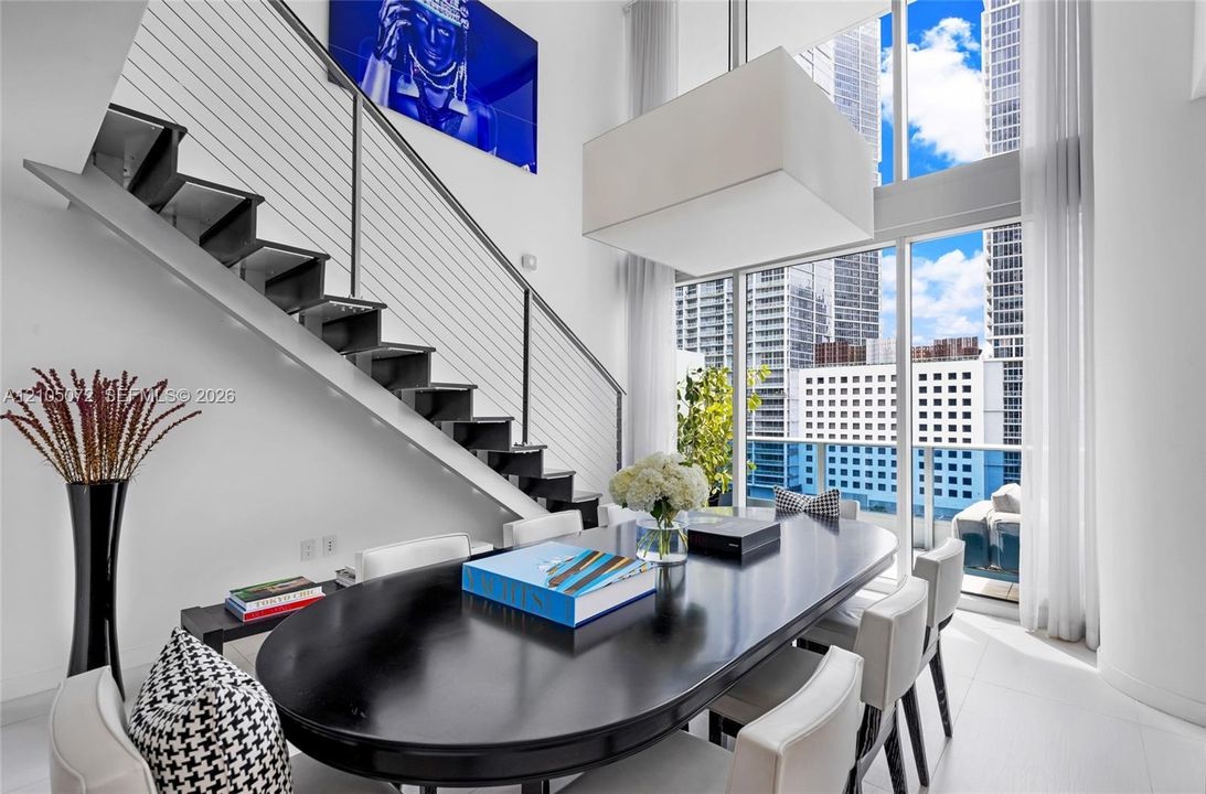 Dining table positioned beneath the cable-railed staircase and double-height windows.
