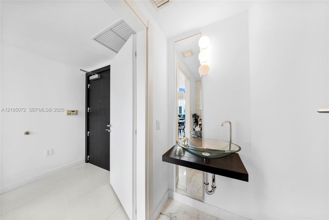 Entry hall with glass vessel sink set on a floating shelf beside the mirror.