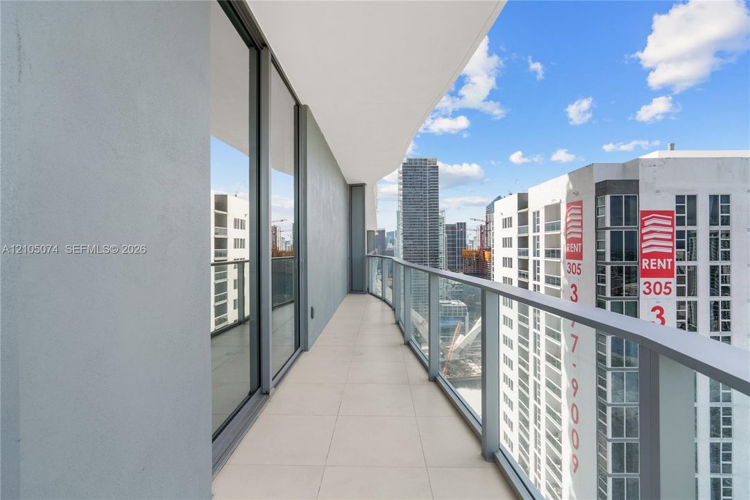 Covered balcony featuring large-format tile flooring, a glass and metal railing system, and floor-to-ceiling sliding glass doors