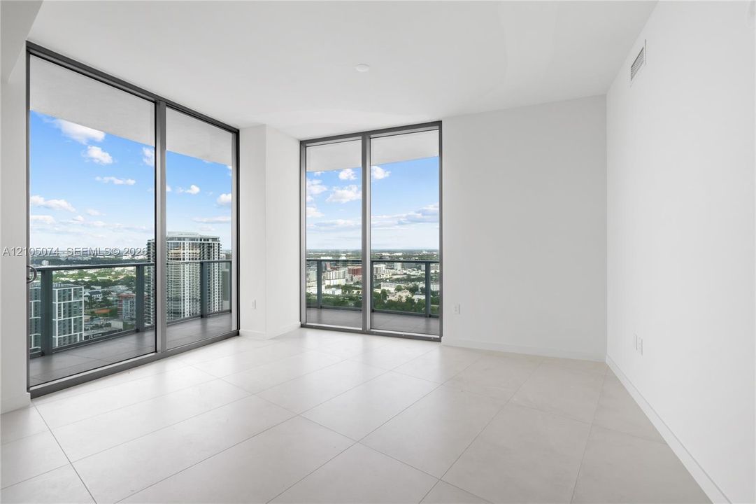 Floor-to-ceiling glass walls, large-format tile flooring, and sliding doors opening to an expansive wrap-around balcony with extensive city scenery