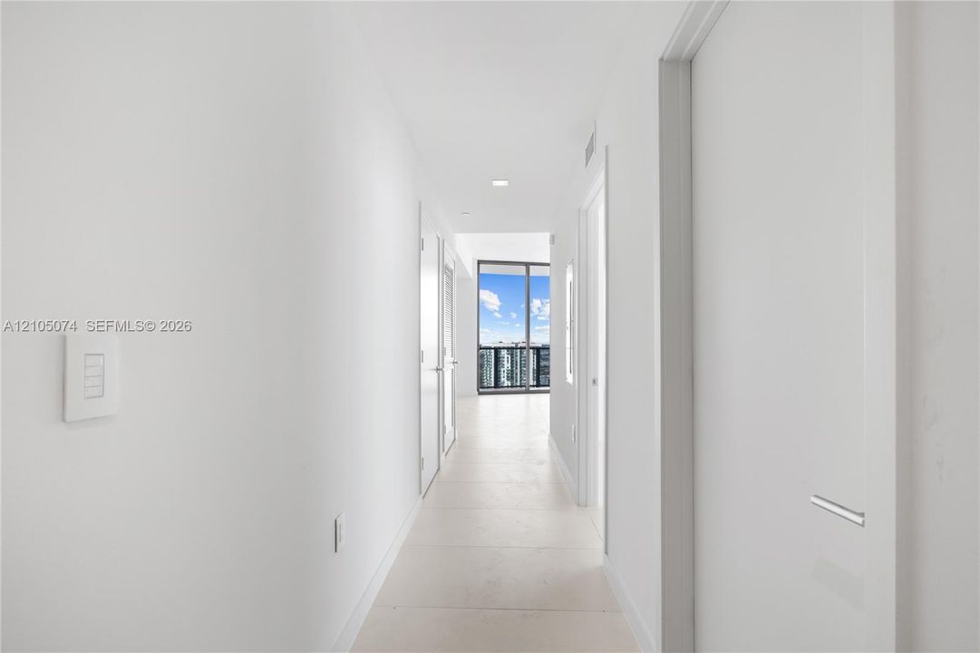 Hallway featuring neutral-toned tile flooring, recessed ceiling lighting, and floor-to-ceiling glass sliding doors