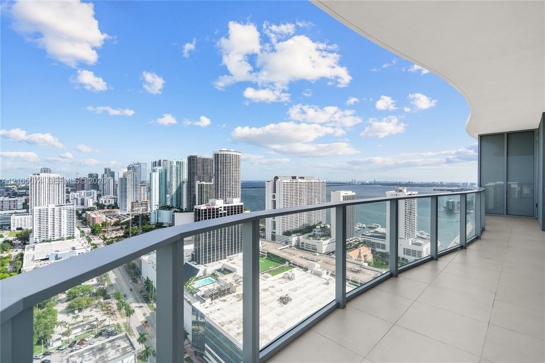 Spacious private balcony with large-format floor tiles and a curved structural design, featuring a glass-panel railing and extensive water and city skyline outlooks