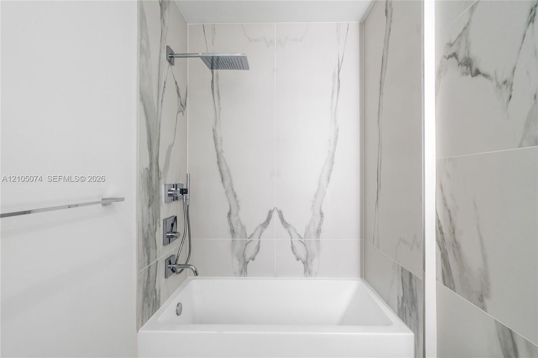 Bathtub featuring large-format veined tile surround, overhead rain shower head, handheld shower wand, and polished chrome fixtures